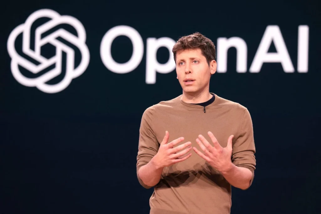 OpenAI CEO speaking on stage in front of the OpenAI logo during a ChatGPT-focused presentation or announcement.
